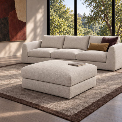 Katrine square ottoman in Field Shell upholstery paired with the matching 3-seater sofa beside garden-facing windows